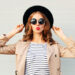Fashion portrait pretty sweet young woman blowing red lips wearing a black hat sunglasses coat over grey background